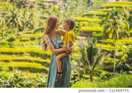 Mom and son on the rice field in the background of rice terraces, Ubud, Bali, Indonesia. Traveling with children concept. Teaching children in practice Mom and son on the rice field in the background of rice terraces, Ubud, Bali, Indonesia. Traveling with children concept. Teaching children in practice 112464755