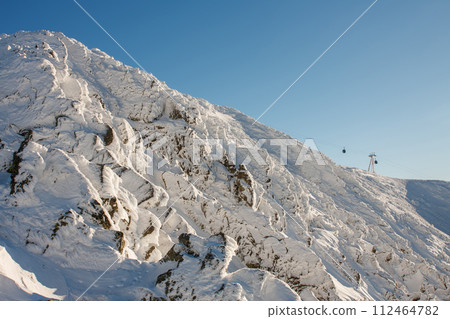 The rocky peak of  mountain Snezka. Winter, morning time, chairlift connecting peak Snezka with town Pec pod Snezkou , krkonose mountain, Czech republic.. 112464782