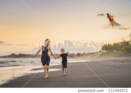 Mom and son are running on the sea beach launching a kite 112464872
