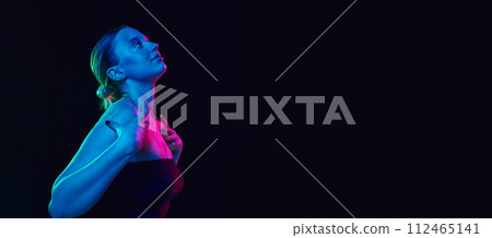 Banner. Side view portrait of young beautiful woman in top looking upwards in neon light against black studio background. Banner. Side view portrait of young beautiful woman in top looking upwards in neon light against black studio background. 112465141