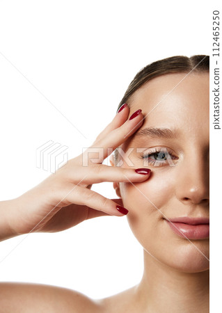 Partial face of young beautiful woman with serene expression, touching her eye area against white studio background. Partial face of young beautiful woman with serene expression, touching her eye area against white studio background. 112465250