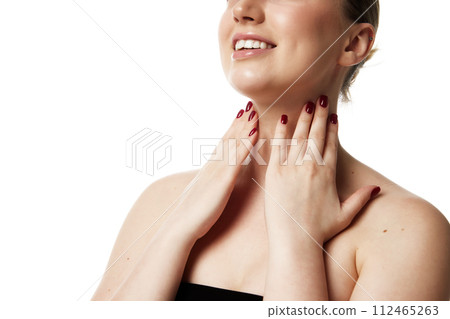 Cropped portrait of woman with radiant smile touching her neck showing effective skincare against white studio background. 112465263