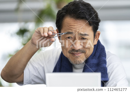 Middle-aged man cutting his eyebrows while looking in the mirror Middle-aged man cutting his eyebrows while looking in the mirror 112465277