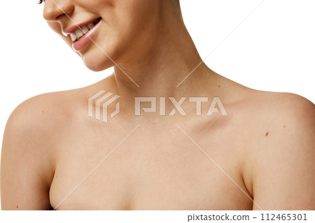 Cropped photo of young female neckline with smooth, healthy skin against white studio background. Model smiling. 112465301