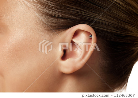 Close up photo of female ear with piercing against white studio background. Plastic injury. Body parts. Close up photo of female ear with piercing against white studio background. Plastic injury. Body parts. 112465307