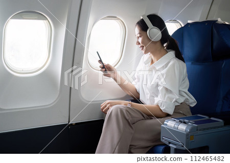 Asian young woman wearing headphone listen to music at first class on airplane during flight, Traveling and Business concept Asian young woman wearing headphone listen to music at first class on airplane during flight, Traveling and Business concept 112465482