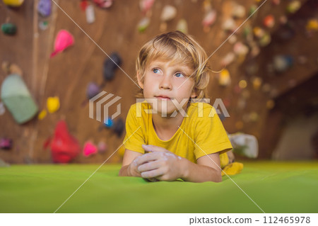 Boy resting after climbing a rock wall indoor Boy resting after climbing a rock wall indoor 112465978