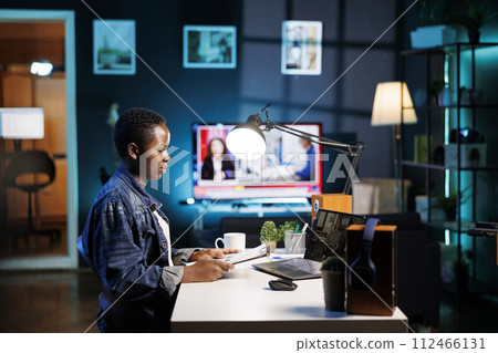 African american college student grasping paperwork while having a conversation through a laptop with female colleague. Two young women having an online discussion, video call on portable computer. African american college student grasping paperwork while having a conversation through a laptop with female colleague. Two young women having an online discussion, video call on portable computer. 112466131