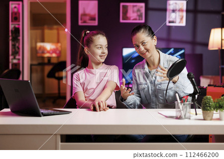 Excited child and her mom do content creation using professional recording equipment to film vlog channel intro. Daughter and parent greet fanbase, presenting today video topic in pink neon studio Excited child and her mom do content creation using professional recording equipment to film vlog channel intro. Daughter and parent greet fanbase, presenting today video topic in pink neon studio 112466200