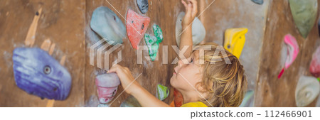little boy climbing a rock wall in special boots. indoor BANNER, LONG FORMAT 112466901