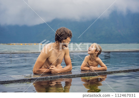Dad and son travelers in Hot Springs in Bali on the background of lake. Traveling with children concept Dad and son travelers in Hot Springs in Bali on the background of lake. Traveling with children concept 112467031