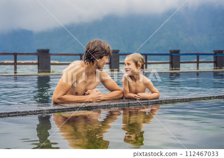Dad and son travelers in Hot Springs in Bali on the background of lake. Traveling with children concept Dad and son travelers in Hot Springs in Bali on the background of lake. Traveling with children concept 112467033