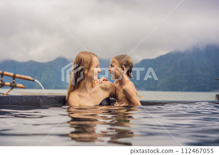 Mom and son travelers in Hot Springs in Bali on the background of lake. Traveling with children concept Mom and son travelers in Hot Springs in Bali on the background of lake. Traveling with children concept 112467055