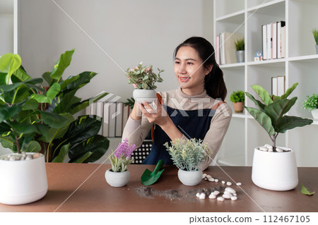 The concept of eco friendly housing, plant care and gardening. Preparing garden. Relax home gardening. Gardener woman asian hand planting flower in pot. Smiling woman takes care of plant 112467105
