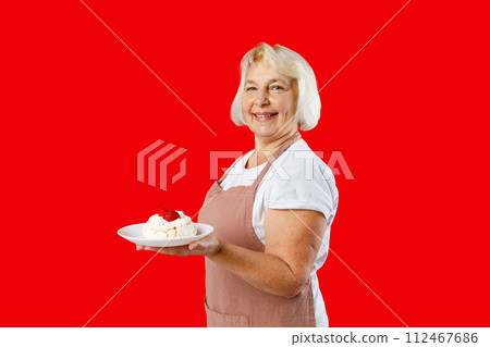 Housewife female chef cook confectioner or baker in apron white t-shirt holding in hand cake on plate isolated on red background in studio. Food concept 112467686