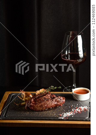 Succulent grilled beef steak with red wine, seasonings, fresh rosemary and grilled vegetables on cutting board Succulent grilled beef steak with red wine, seasonings, fresh rosemary and grilled vegetables on cutting board 112469085