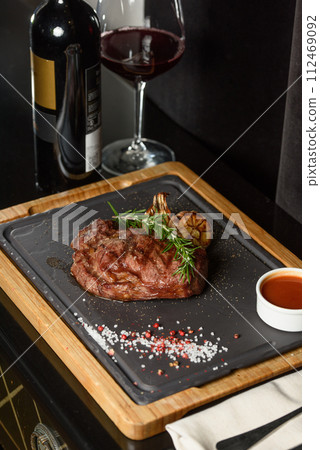 Succulent grilled beef steak with red wine, seasonings, fresh rosemary and grilled vegetables on cutting board Succulent grilled beef steak with red wine, seasonings, fresh rosemary and grilled vegetables on cutting board 112469092