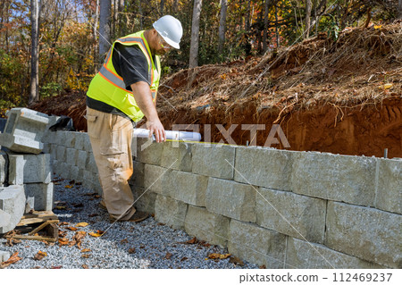 Worker studied blueprint plans when mounting retaining walls using cement blocks Worker studied blueprint plans when mounting retaining walls using cement blocks 112469237