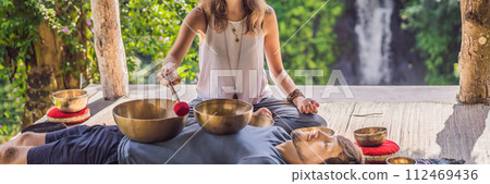 BANNER, LONG FORMAT Nepal Buddha copper singing bowl at spa salon. Young beautiful man doing massage therapy singing bowls in the Spa against a waterfall. Sound therapy, recreation, meditation 112469436