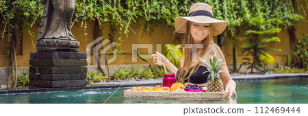 BANNER, LONG FORMAT Breakfast tray in swimming pool, floating breakfast in luxury hotel. Girl relaxing in the pool drinking smoothies and eating fruit plate, smoothie bowl by the hotel pool. Exotic 112469444