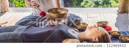 BANNER, LONG FORMAT Nepal Buddha copper singing bowl at spa salon. Young beautiful woman doing massage therapy singing bowls in the Spa against a waterfall. Sound therapy, recreation, meditation 112469452