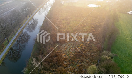 Misty Aerial View of a Lush Canal Path at Sunrise Misty Aerial View of a Lush Canal Path at Sunrise 112470040