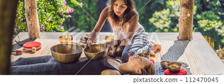 BANNER, LONG FORMAT Nepal Buddha copper singing bowl at spa salon. Young beautiful woman doing massage therapy singing bowls in the Spa against a waterfall. Sound therapy, recreation, meditation 112470045