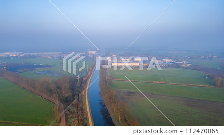 Elevated View of Misty Canal Dividing Rural Farmland and Industrial Estate 112470065