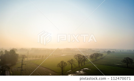 Soft Dawn Light Over a Misty Rural Landscape with Scattered Trees Soft Dawn Light Over a Misty Rural Landscape with Scattered Trees 112470071