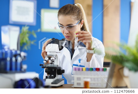 Woman scientist chemist looking through microscope and holding test tube Woman scientist chemist looking through microscope and holding test tube 112470666