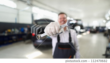 Male repairman holding wrench in car workshop closeup Male repairman holding wrench in car workshop closeup 112470682