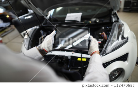 Master repairman holding digital tablet near open hood of car closeup Master repairman holding digital tablet near open hood of car closeup 112470685