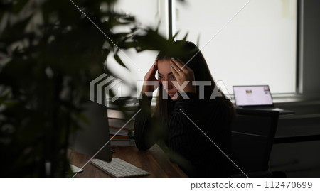 Tired woman holding her head with hands in front of computer screen in office Tired woman holding her head with hands in front of computer screen in office 112470699