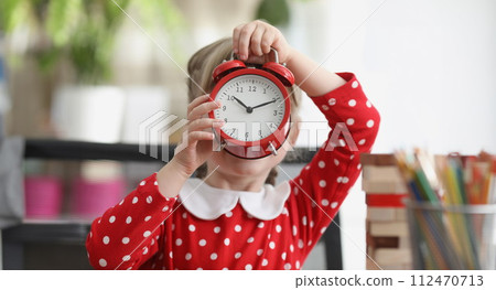 Little girl holding red alarm clock in front of her face Little girl holding red alarm clock in front of her face 112470713
