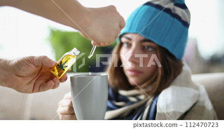 Drops of marijuana oil dripping into cup of sick woman wearing hat closeup Drops of marijuana oil dripping into cup of sick woman wearing hat closeup 112470723