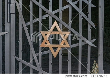 A jewish Star of David, made of golden metal on a black metal fence Dachau 112470755