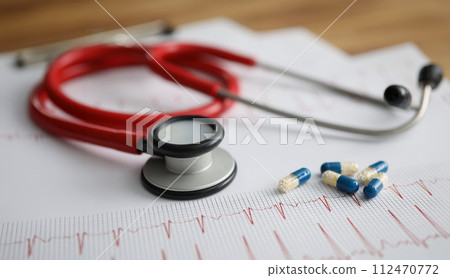 Medical capsules and red stethoscope lying on electrocardiogram closeup 112470772