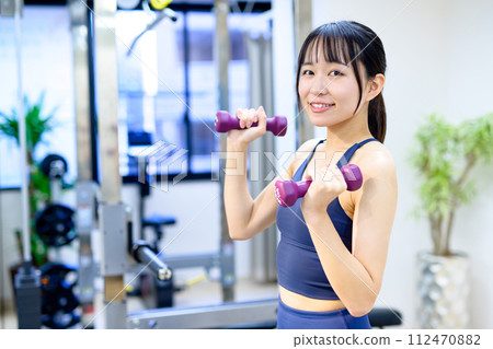 一位年輕女子在私人健身房訓練身體,使用啞鈴、二頭肌、肌肉訓練女孩 一位年輕女子在私人健身房訓練身體,使用啞鈴、二頭肌、肌肉訓練女孩 112470882