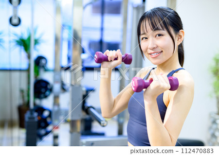A young woman training her body at a personal gym, using dumbbells, biceps, muscular training girl A young woman training her body at a personal gym, using dumbbells, biceps, muscular training girl 112470883