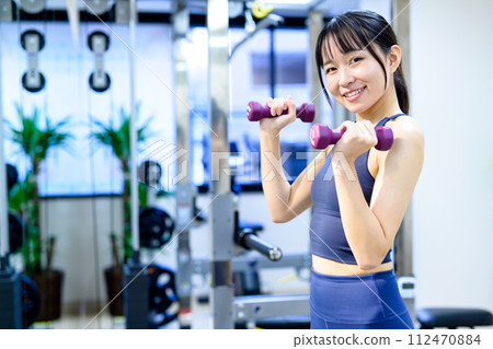 A young woman training her body at a personal gym, using dumbbells, biceps, muscular training girl 112470884