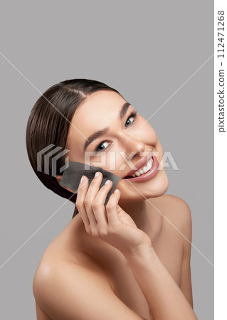 Face skin care. Smiling woman using facial oil blotting paper portrait. Closeup of beautiful happy girl model with natural makeup using oil absorbing sheets, beauty product Face skin care. Smiling woman using facial oil blotting paper portrait. Closeup of beautiful happy girl model with natural makeup using oil absorbing sheets, beauty product 112471268