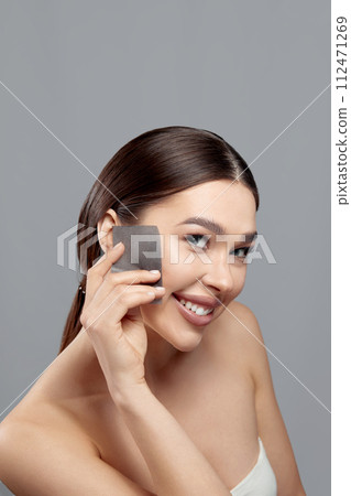 Beautiful woman using facial oil blotting paper. Photo of woman with perfect makeup on gray background. Beauty concept. Cosmetology, cosmetics. Facial treatment Beautiful woman using facial oil blotting paper. Photo of woman with perfect makeup on gray background. Beauty concept. Cosmetology, cosmetics. Facial treatment 112471269