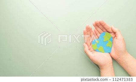 World heart day. Flat lay of hands holding heart shape with earth map made by paper on green background. Template for cardiology medical care, earth's day celebration, love and save the earth. 112471383