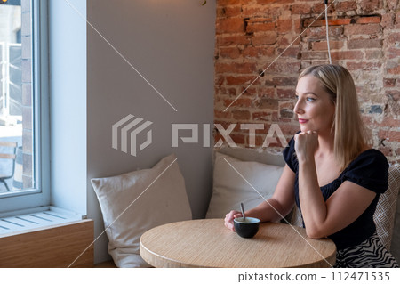 Contemplative Young Woman Enjoying Coffee in a Chic Cafe 112471535