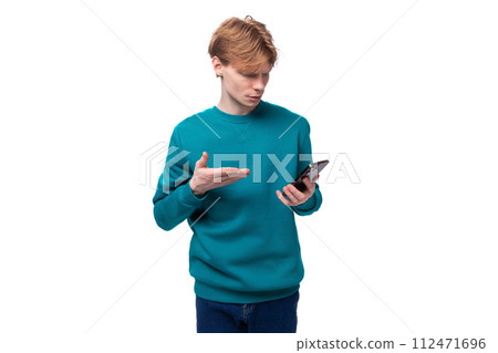 young cute man with red hair dressed in a blue sweater is outraged while reading messages on the 112471696