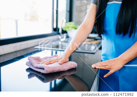 A cheerful housewife diligently cleans her kitchen table with a rag and detergent, emphasizing safety and hygiene. Illustrating routine household chores for a sanitized home. Wiping cloth kitchen A cheerful housewife diligently cleans her kitchen table with a rag and detergent, emphasizing safety and hygiene. Illustrating routine household chores for a sanitized home. Wiping cloth kitchen 112471992