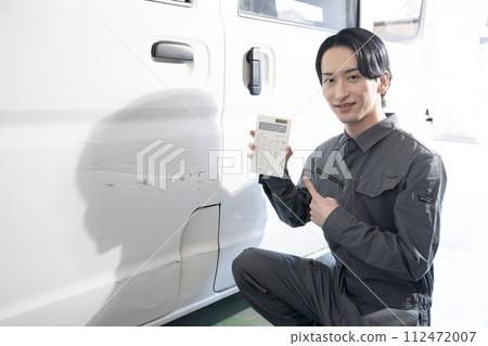 一名工人正在估算修理受損汽車的費用 一名工人正在估算修理受損汽車的費用 112472007