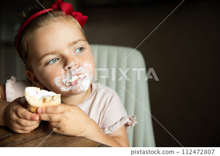 Portrait of little beautiful girl who sits table at home and eats delicious ice cream in waffle cup Portrait of little beautiful girl who sits table at home and eats delicious ice cream in waffle cup 112472807