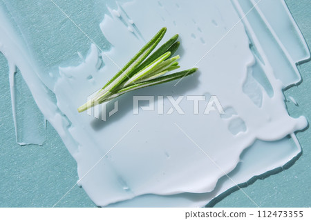 A smear of white cream with a sprig of rosemary on a blue background. 112473355