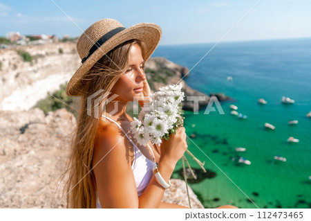 Woman travel sea. Happy woman in a beautiful location poses on a cliff high above the sea, with emerald waters and yachts in the background, while sharing her travel experiences 112473465